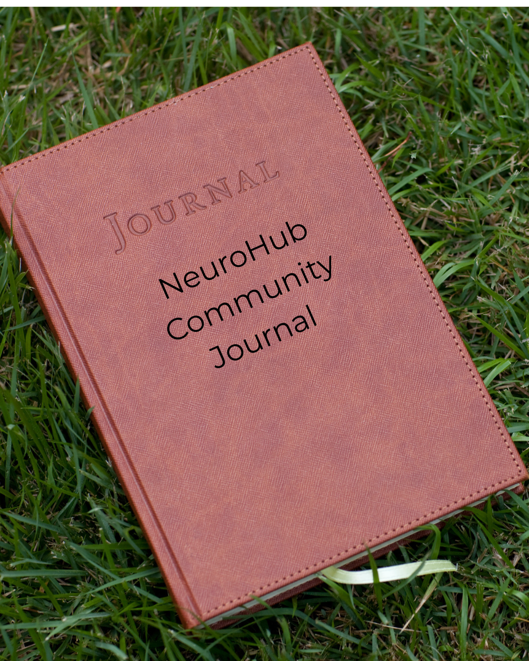 A rust-brown leather-textured notebook lies at an angle on fresh green grass. Its cover has the word Journal embossed in capital letters, with stitched edges around the border. Across the middle, black text reads NeuroHub Community Journal. A pale green ribbon bookmark peeks out from between the cream pages at the bottom edge.